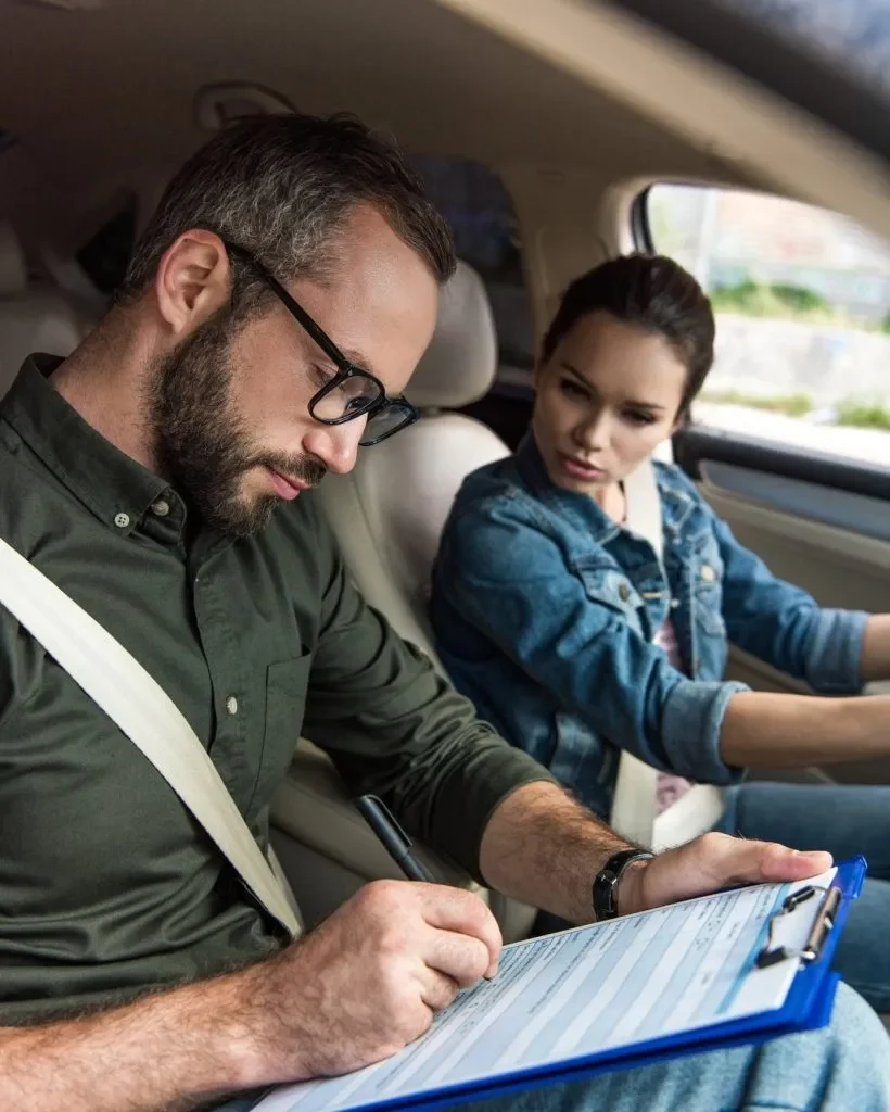 Instructeur d'auto-école vérifiant une fiche pendant une leçon de conduite avec une élève concentrée